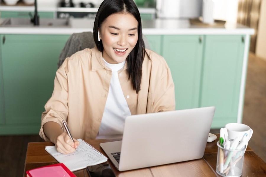 woman using laptop while taking notes